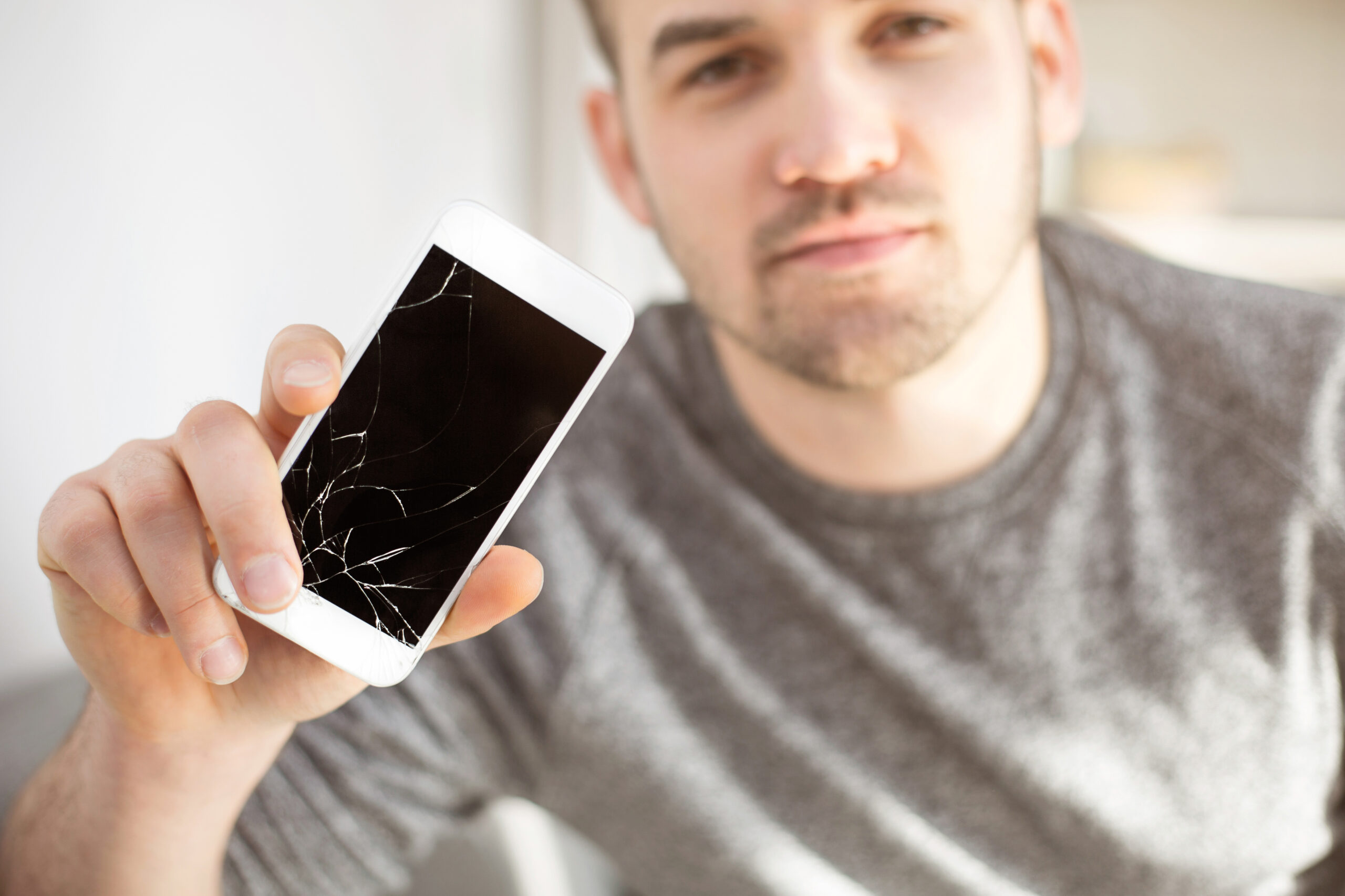 A man holding up a broken cell phone in need of repair.