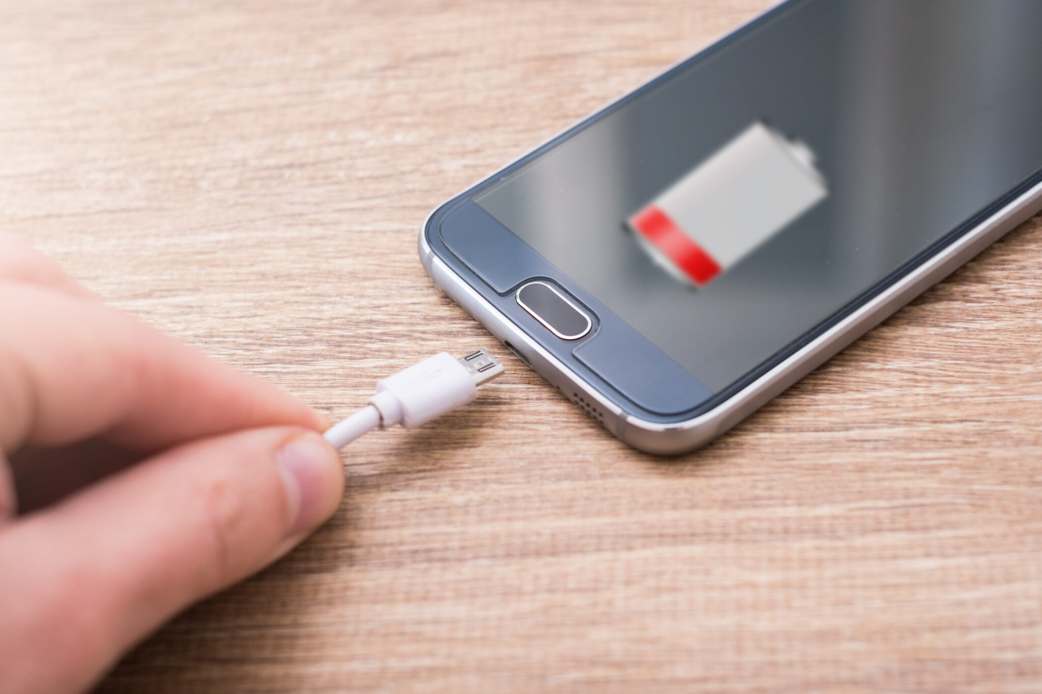 A person is charging a phone with a battery attached to it for Houston phone repair.