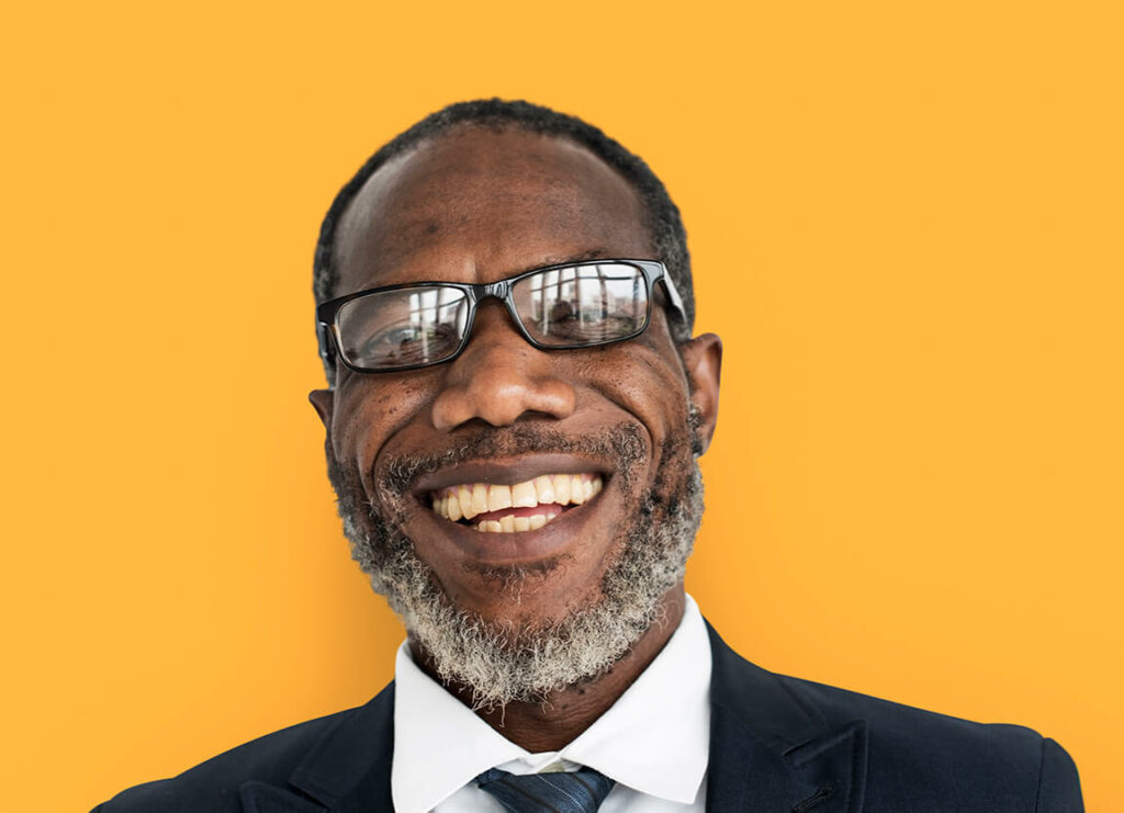 A black man wearing glasses and a suit is smiling against a yellow background, offering Houston phone repair services.