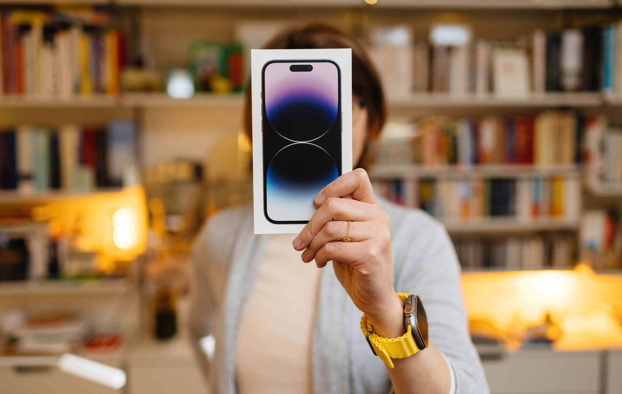 A woman holds up an iPhone for repair in front of a bookcase.